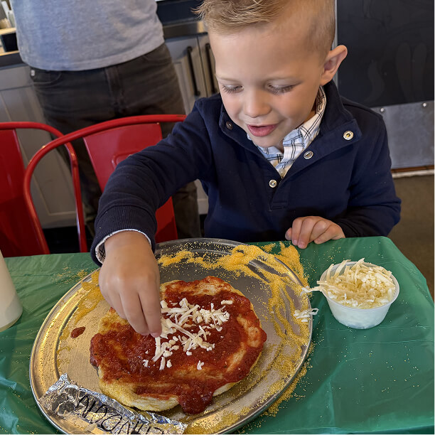 Child placing cheese shreds on his personal pizza