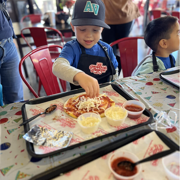 Child putting cheese shreds on his personal pizza